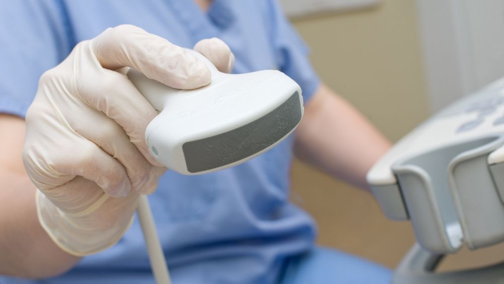 A nurse is holding an ultrasound probe in her hand.