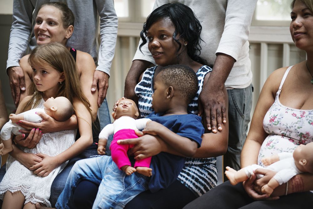A group of people are sitting next to each other holding dolls.