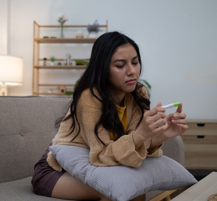 Woman sitting on a couch, looking at a pregnancy test in her hands in a cozy living room