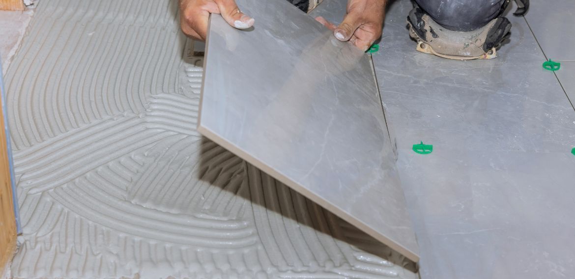 Person installing a tile floor, applying a tile to mortar.