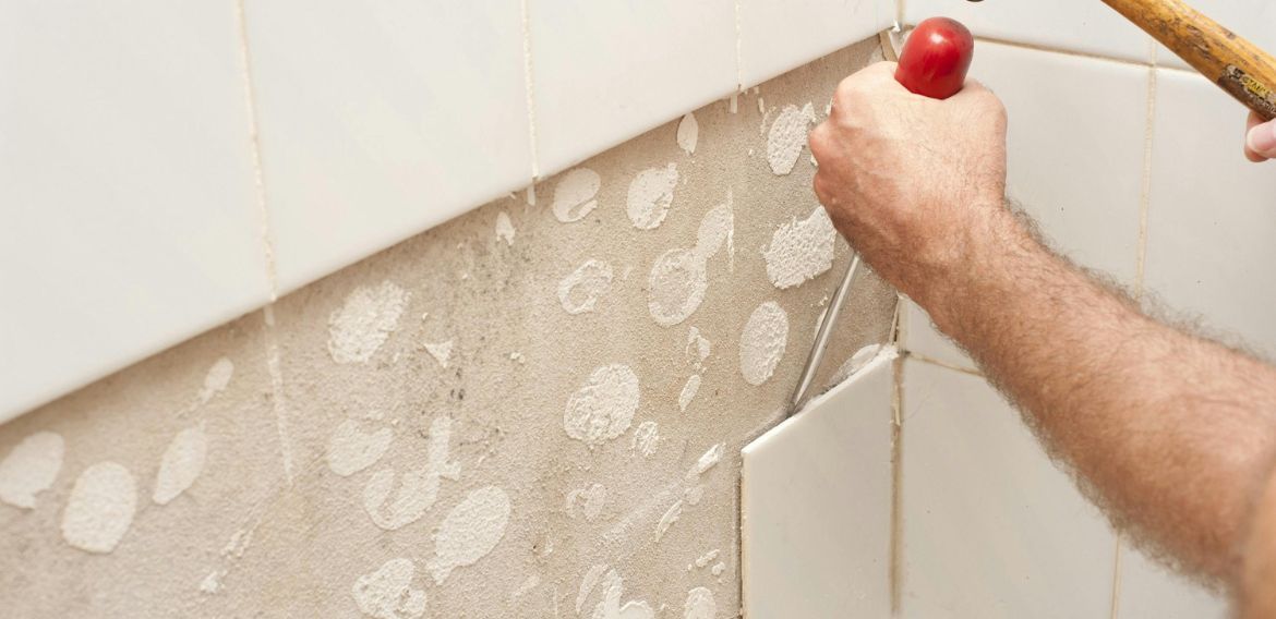 A person using a chisel and hammer to remove tiles from a wall.