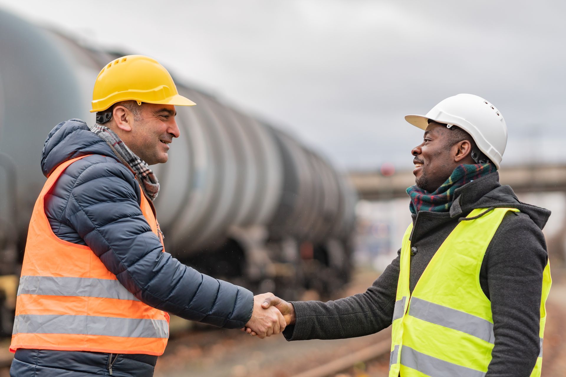 Two construction workers are shaking hands in front of a train.