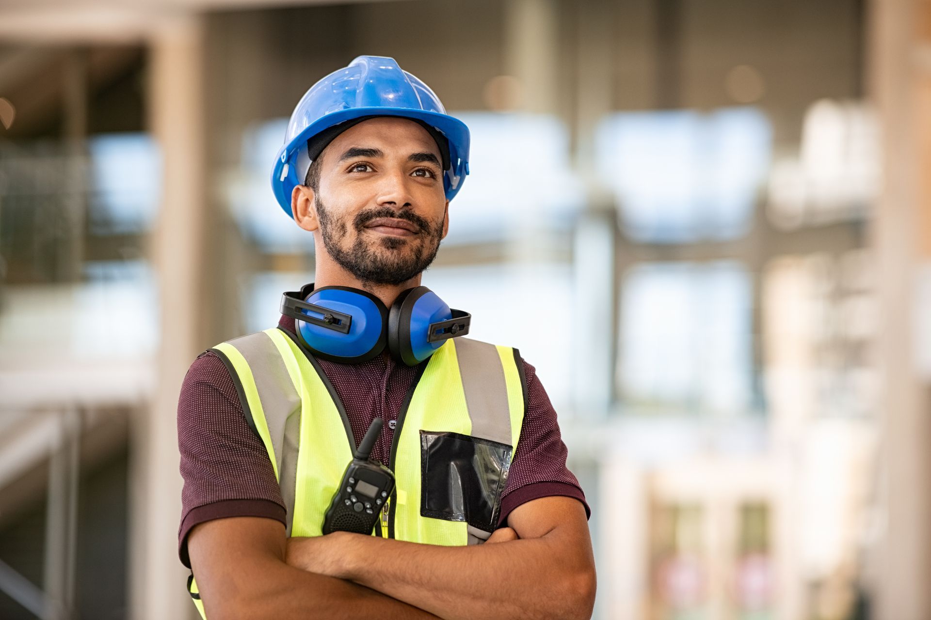 A man wearing a hard hat and headphones is standing with his arms crossed.