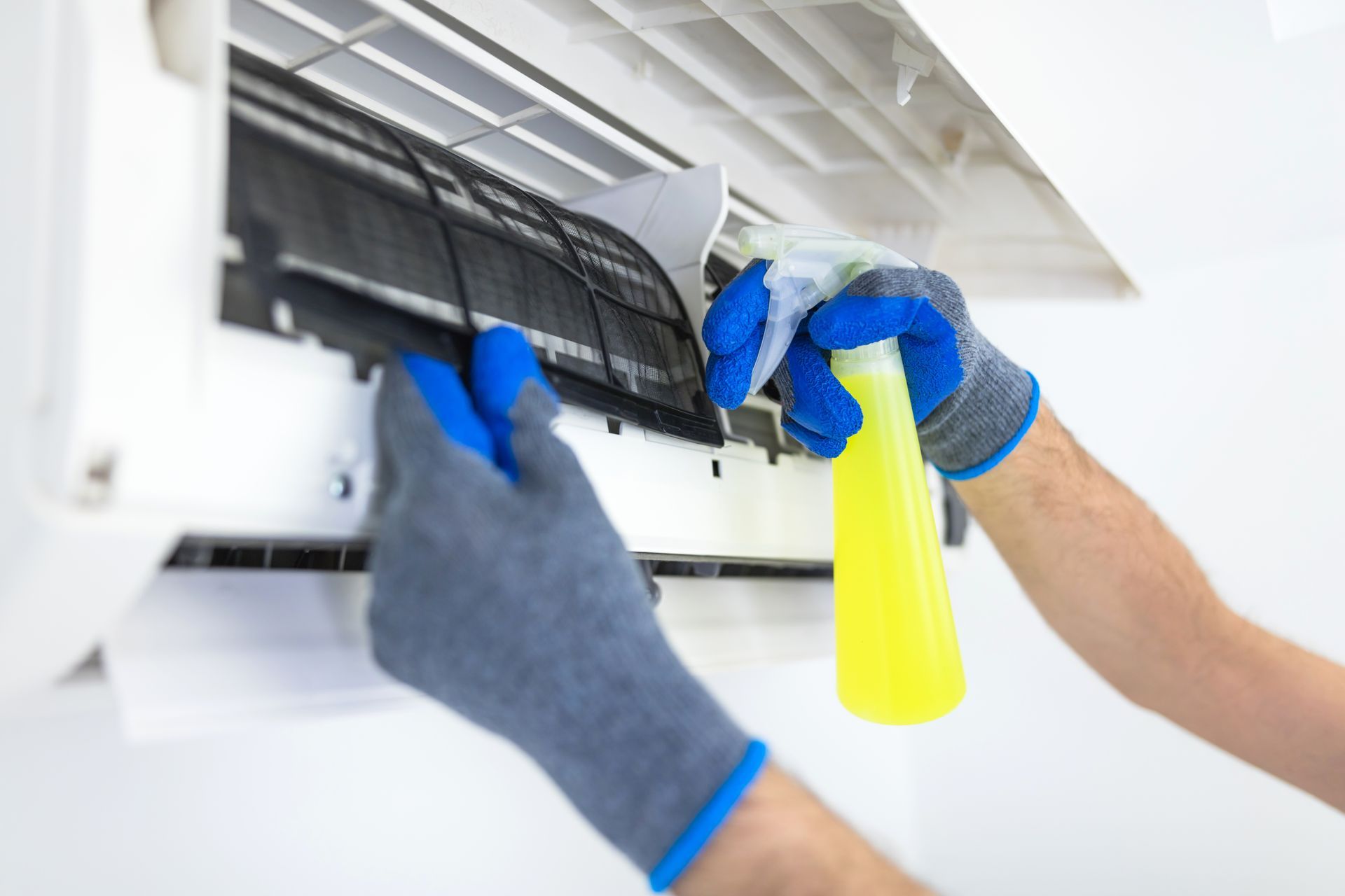 Person cleaning an air conditioner filter with a spray bottle and gloves.