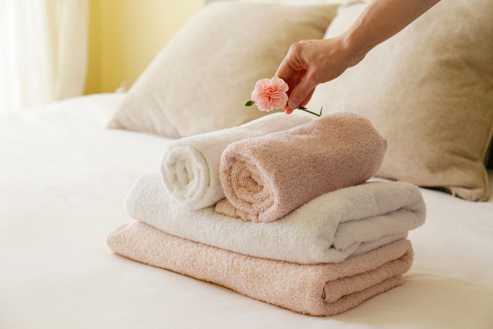 A Person Is Holding A Flower Over A Stack Of Towels On A Bed — Buderim Laundrette In Buderim, QLD