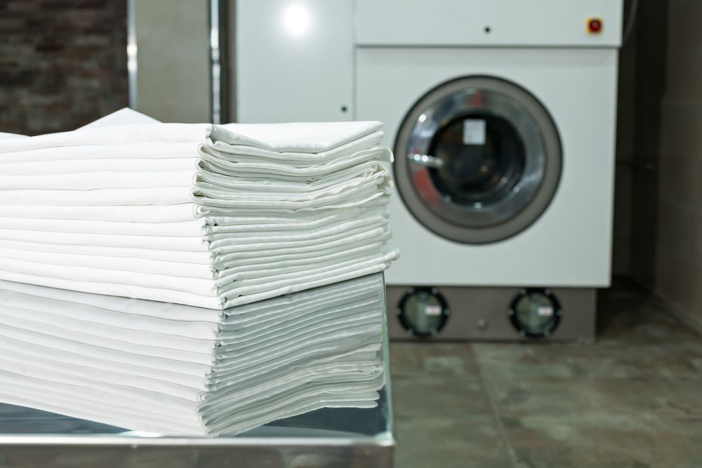 A Stack Of Towels Sits Next To A Washing Machine — Buderim Laundrette In Buderim, QLD