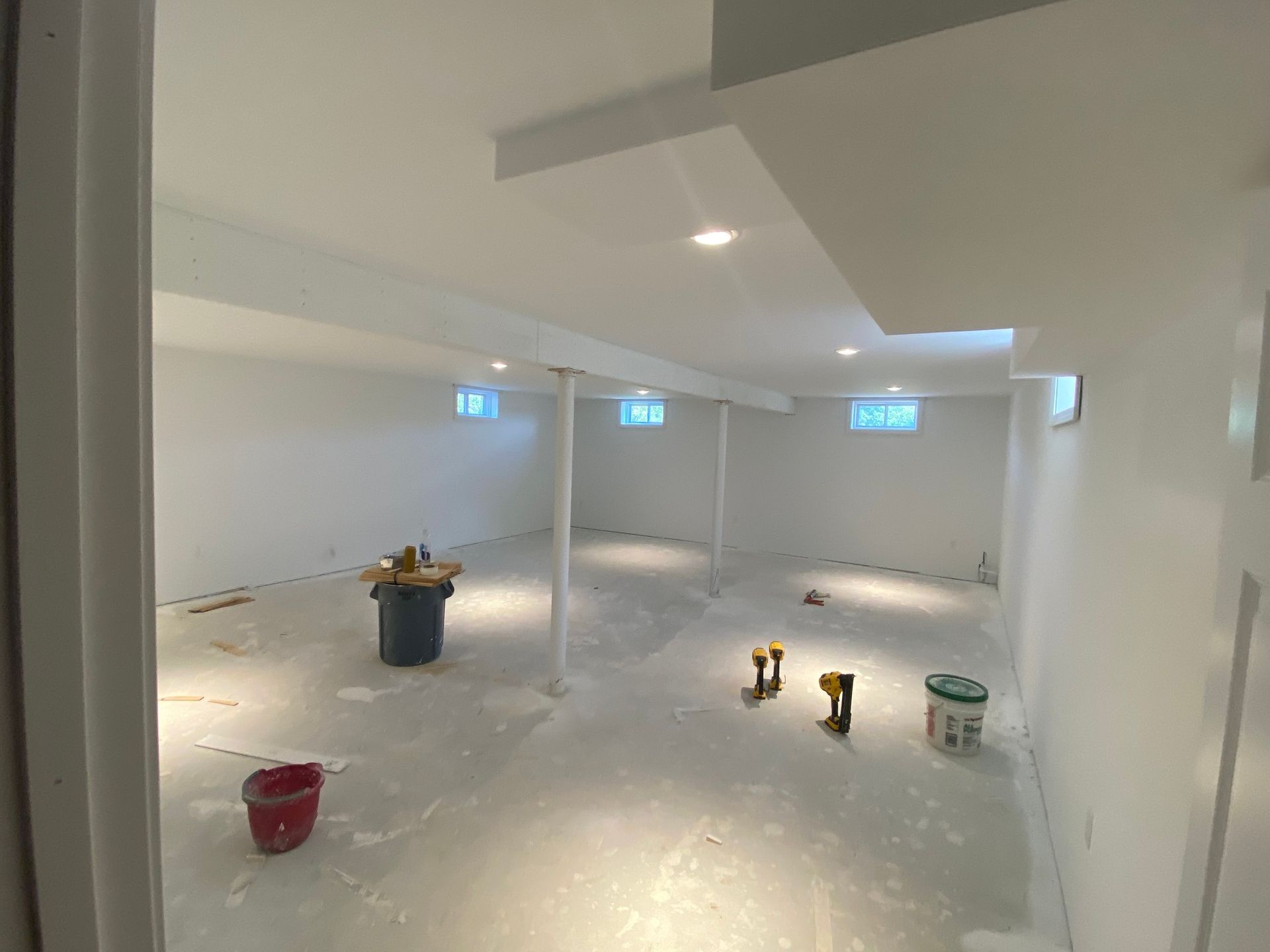 An empty basement with white walls and a bucket on the floor.