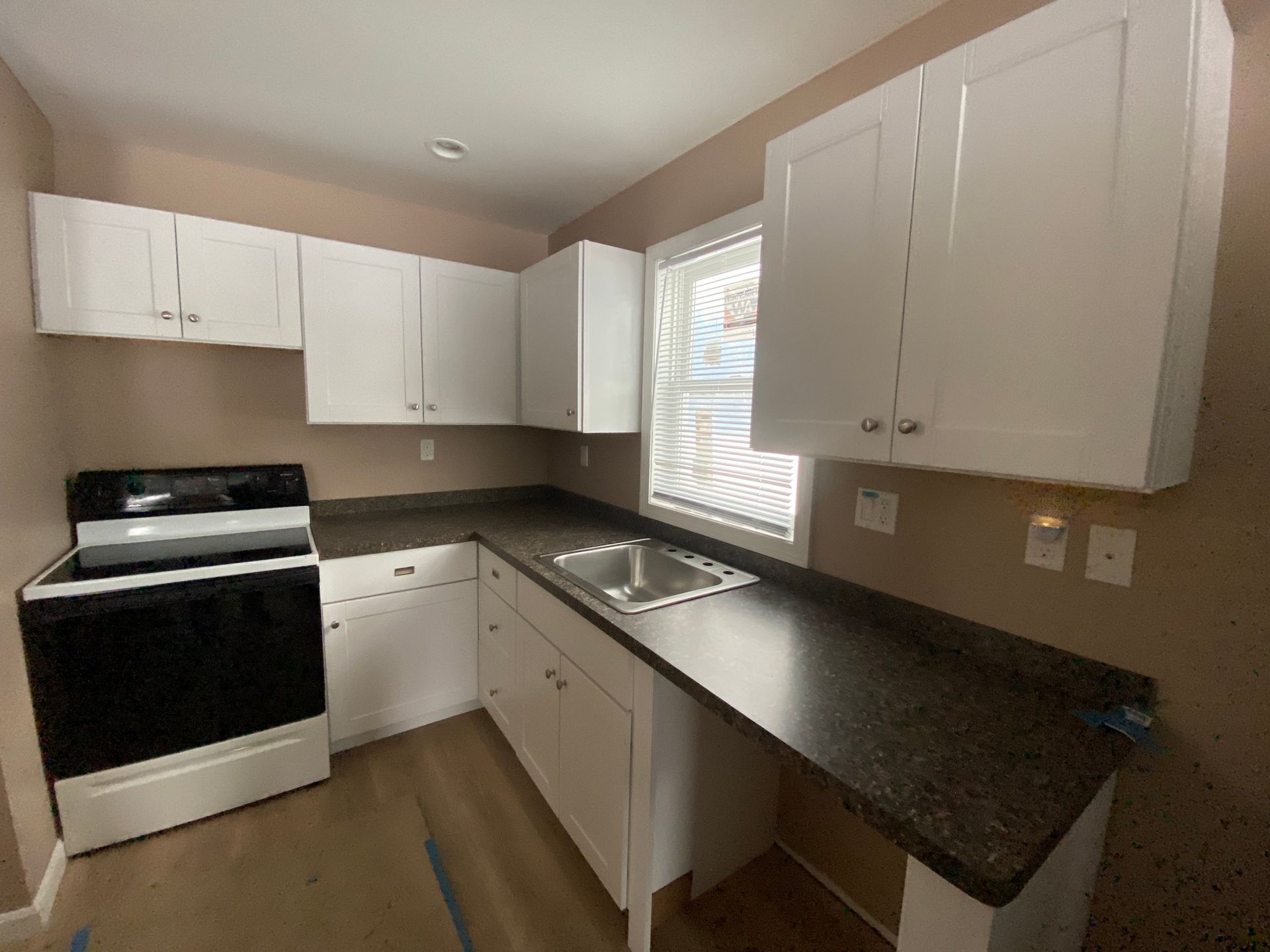 A kitchen with white cabinets , a black stove , a sink and a window.