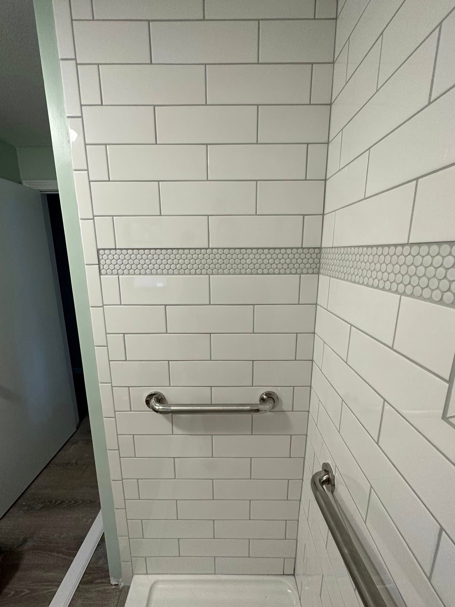 A bathroom with white tiles and a stainless steel railing.