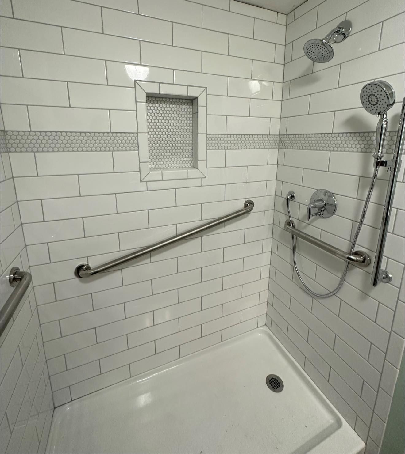 A bathroom with white brick walls and a walk in shower with a hand rail.