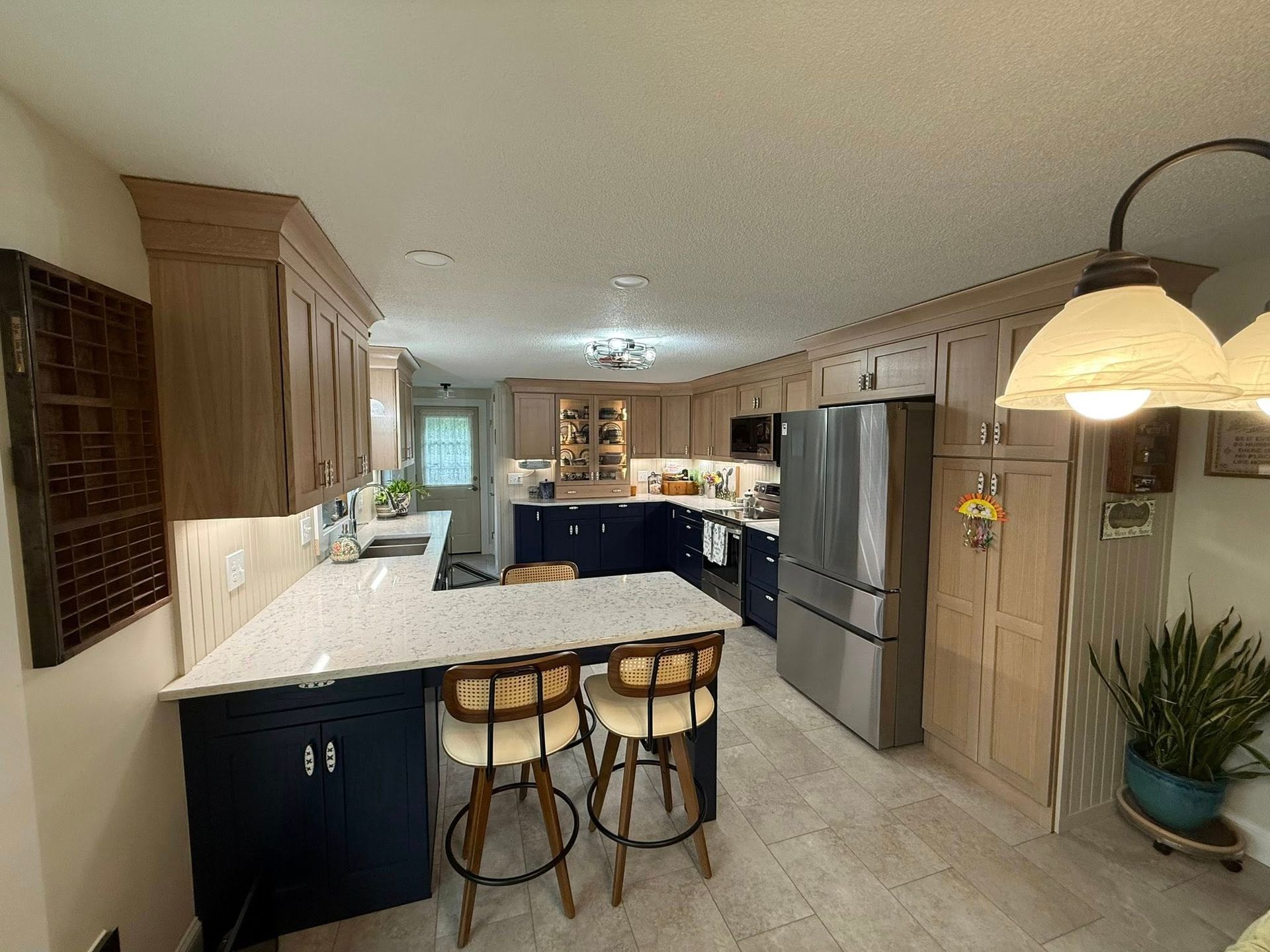 Kitchen with light wood cabinets, dark blue island, stainless steel refrigerator, and breakfast bar with stools.