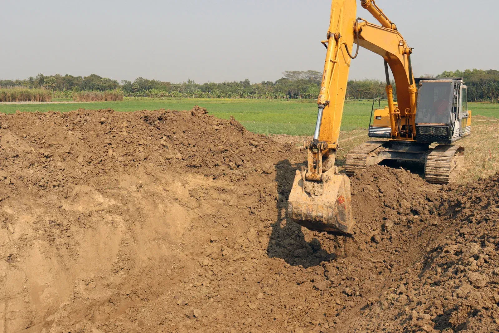 A yellow excavator is digging a hole in a field.