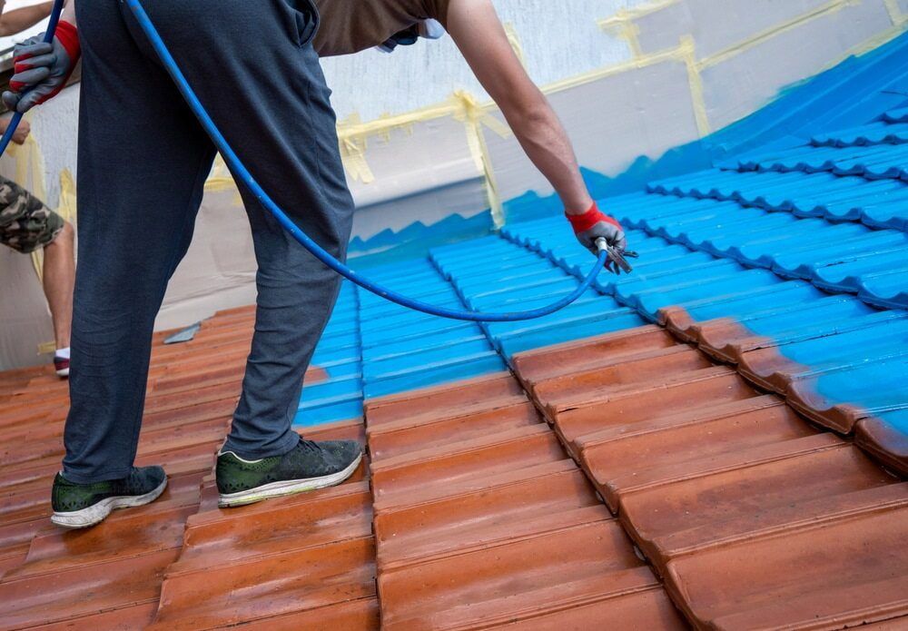 A Man is Spraying Blue Paint on a Tiled Roof — Cornall Painting Services in Lake Cathie, NSW 