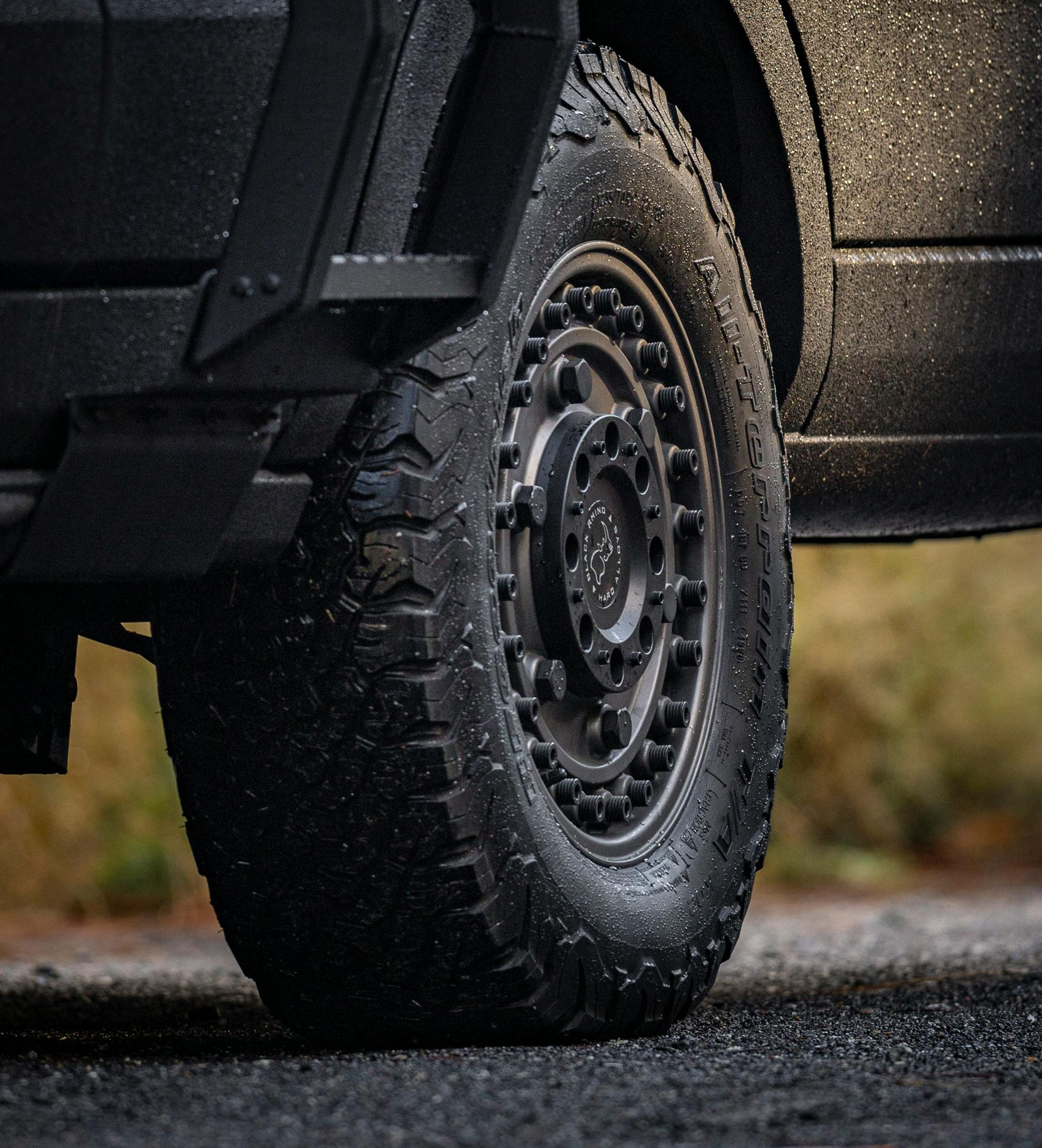 Mechanic in blue jumpsuit tightening lug nuts on a car tire in a garage.