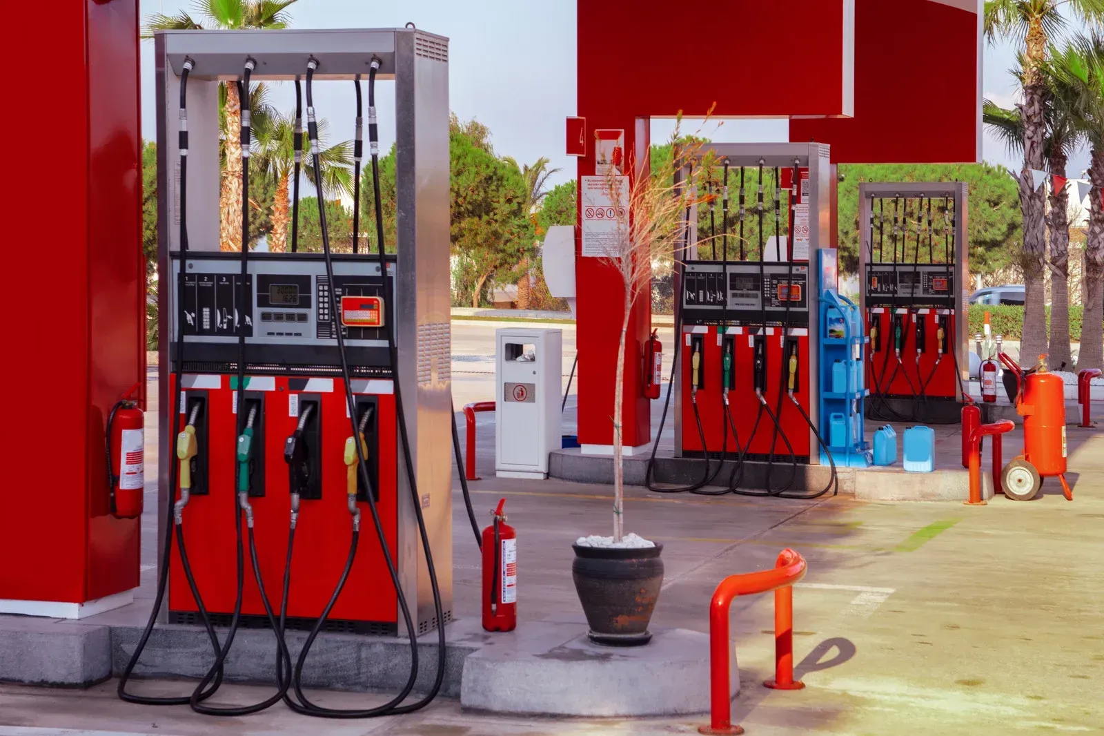 Red and silver gas pumps at a gas station with palm trees in the background.