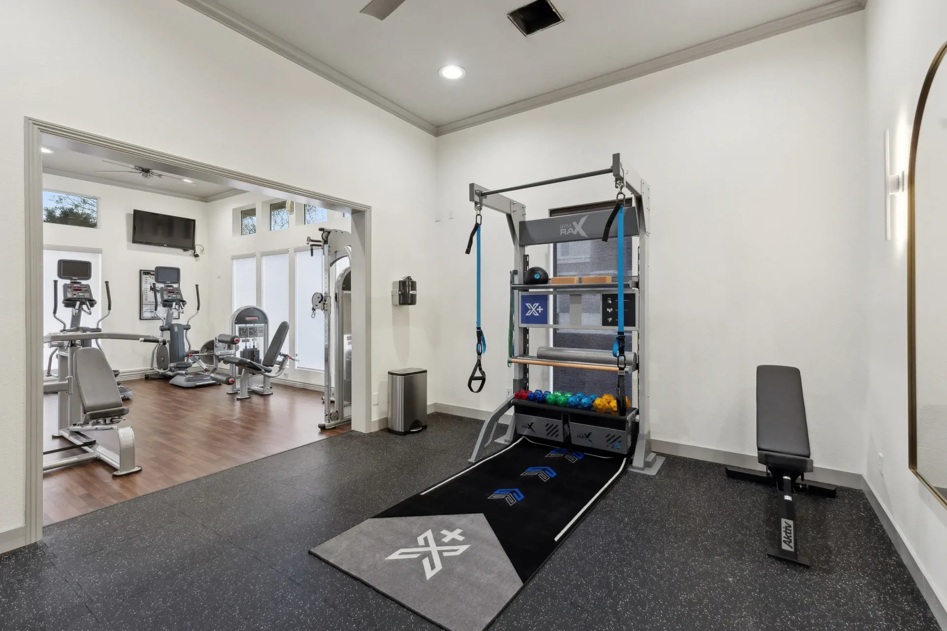 Interior view of a modern gym with cardio machines and a weight rack.