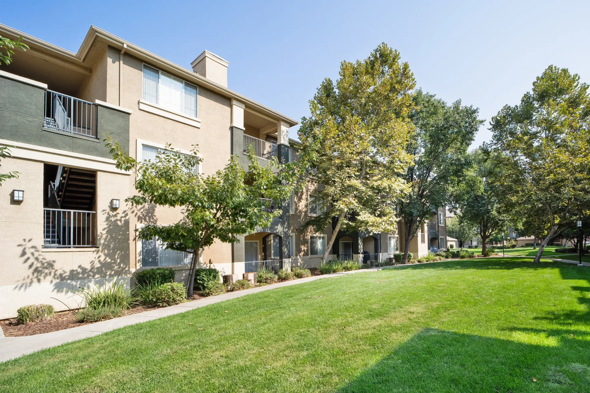 Exterior view of a modern apartment community with a grassy lawn and trees.