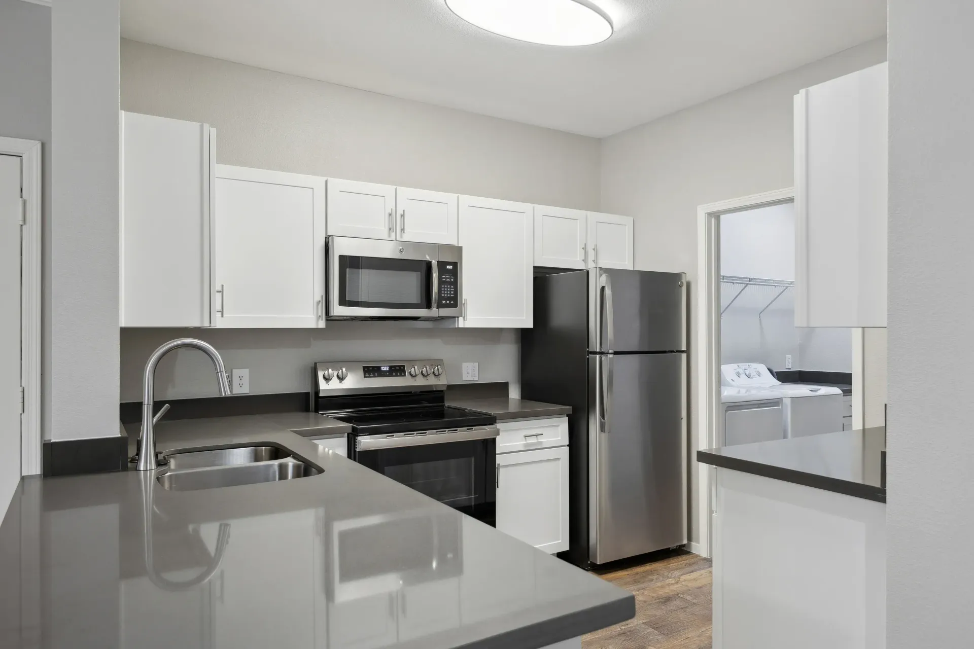 Modern apartment kitchen with white cabinets, gray countertops, and stainless steel appliances.