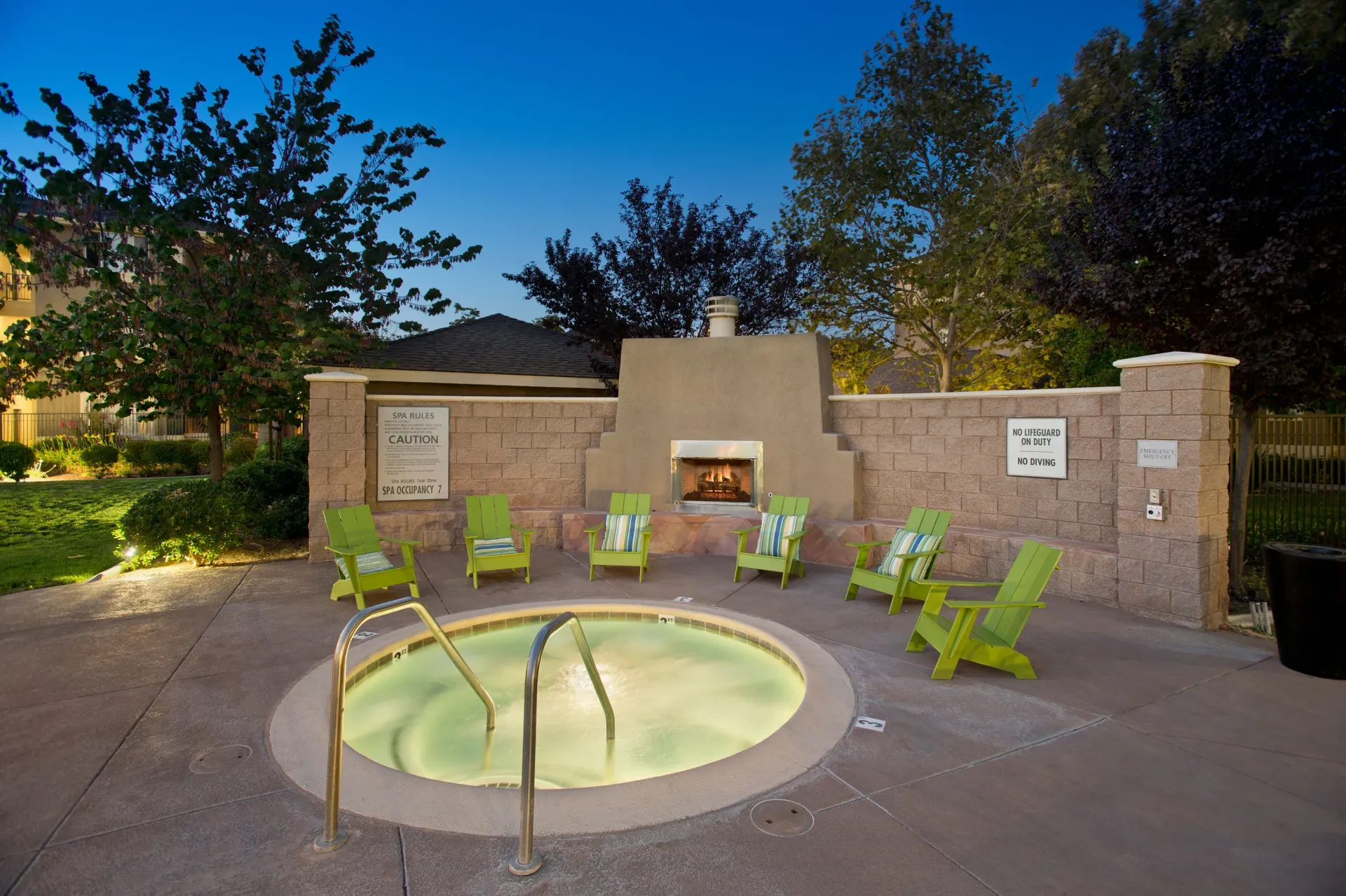 Outdoor hot tub surrounded by lime-green chairs and a central fireplace.