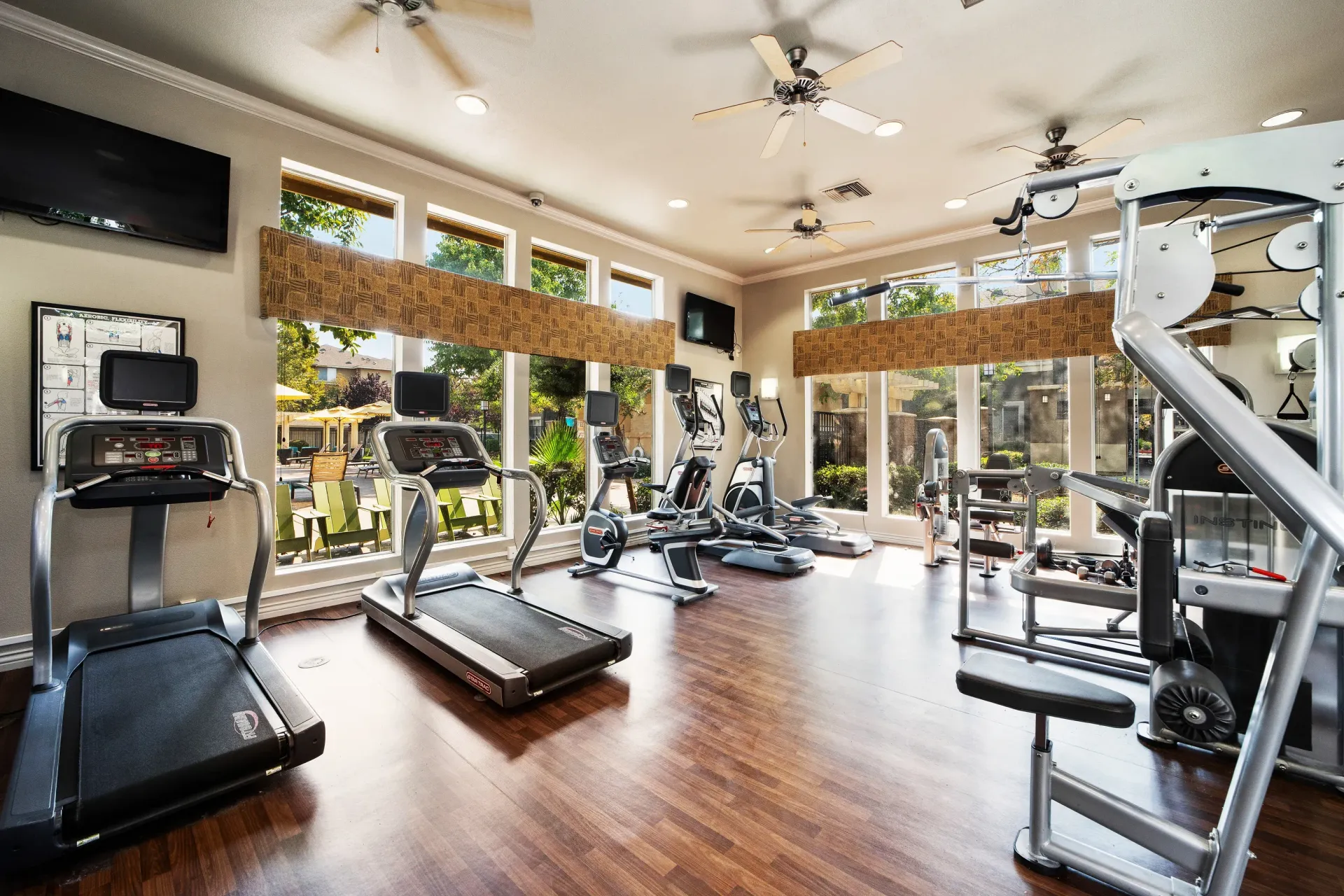 Interior of a community gym with cardio machines and large windows.