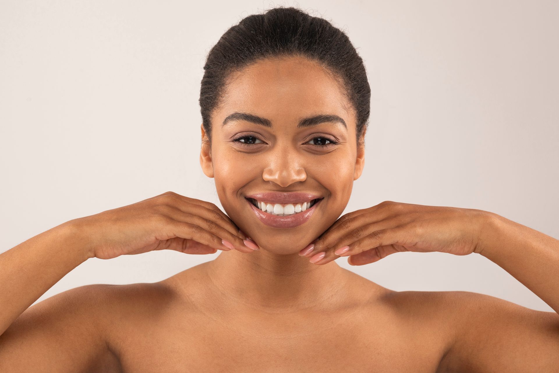 a woman is smiling and touching her face with her hands .