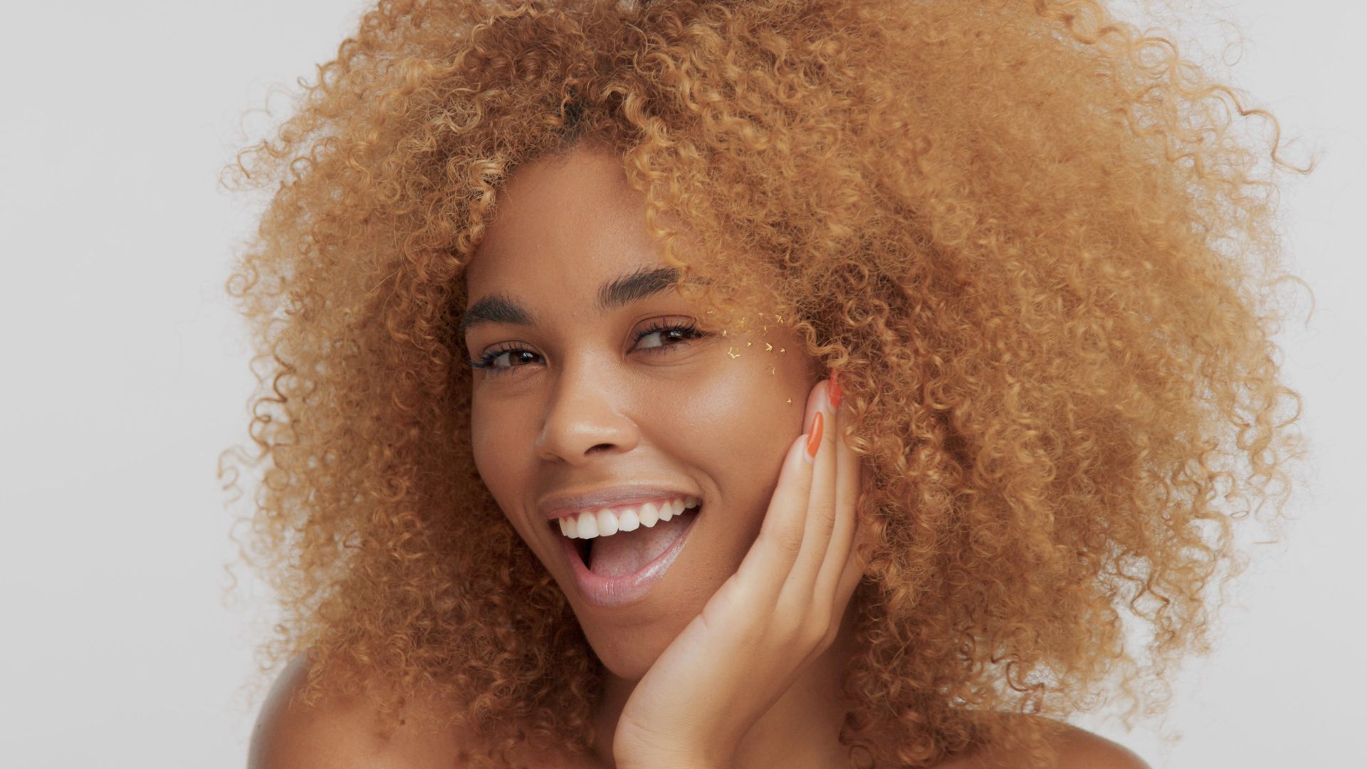 a woman with curly hair is smiling and touching her face .