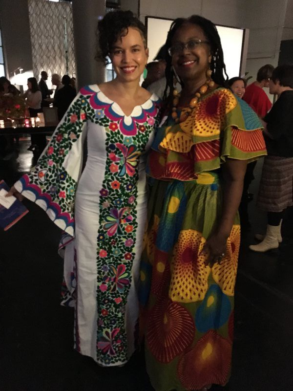 Two women in colorful dresses pose together at an event.