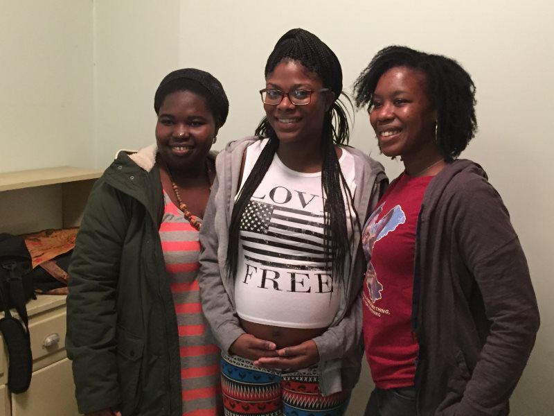 Three people smiling, posing together indoors. One wears a shirt that says 
