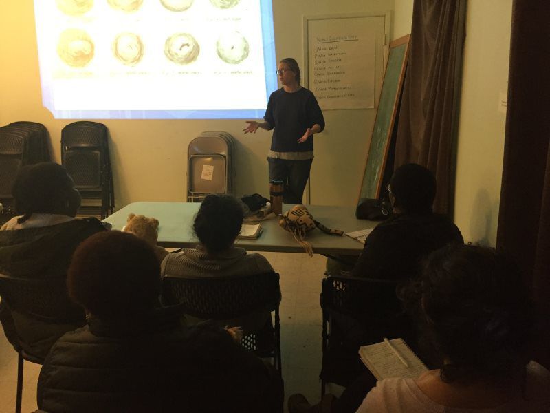 A woman presenting a slideshow to a group in a dimly lit room.