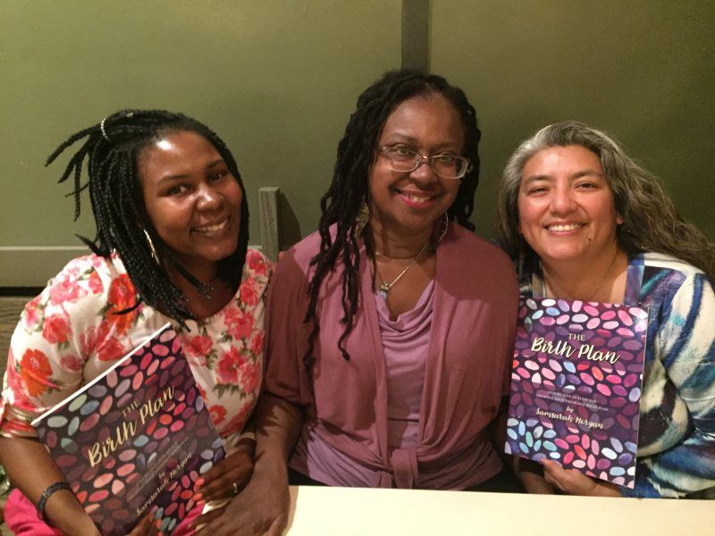 Three smiling women hold books, titled 