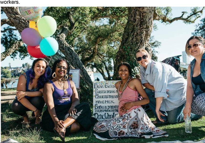 Group of people celebrating outdoors; balloons, sign, happy expressions.