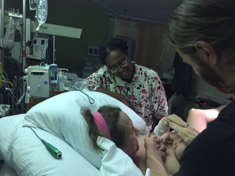 Woman in bed giving birth, with medical staff assisting in a hospital room.