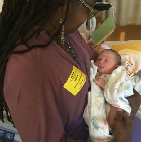 Woman holding newborn baby, in hospital room; baby wrapped in blanket, woman wearing visitor badge.