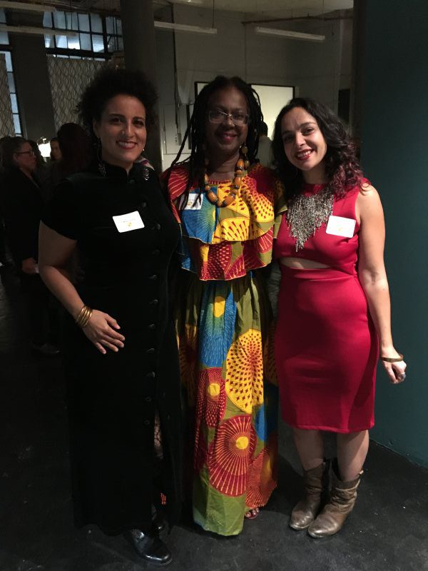 Three people pose together. One in a black dress, one in a colorful maxi dress, and one in a red dress.