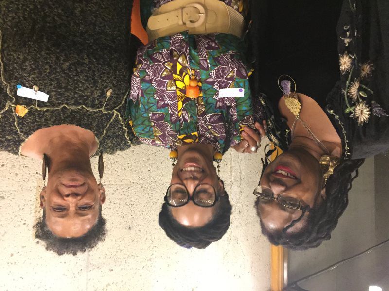 Three people smiling, posing together. Dark clothing, name tags, interior setting.