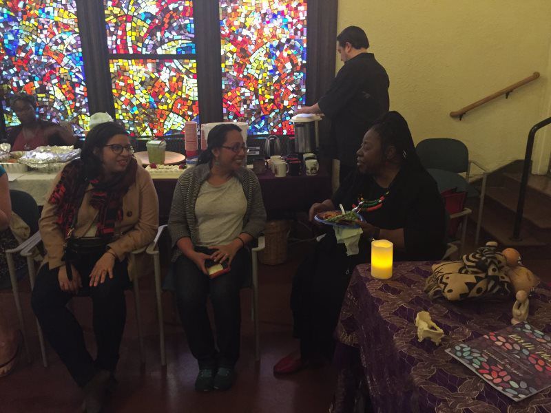 People chatting at a table with a candle, in front of a stained glass window.