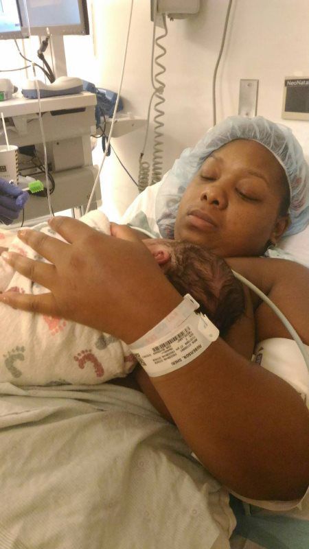New mother resting with newborn baby in a hospital bed.