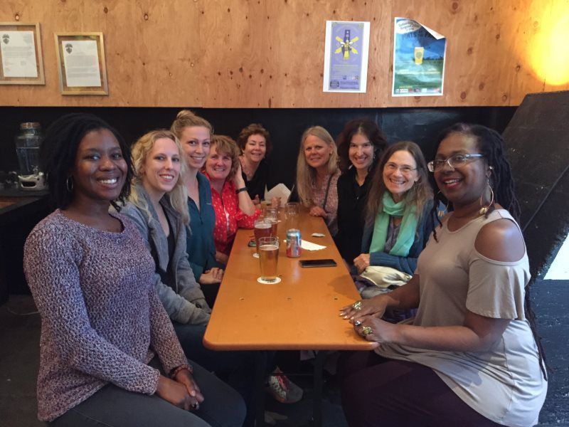 Group of women smiling at a table inside a bar. They have drinks.