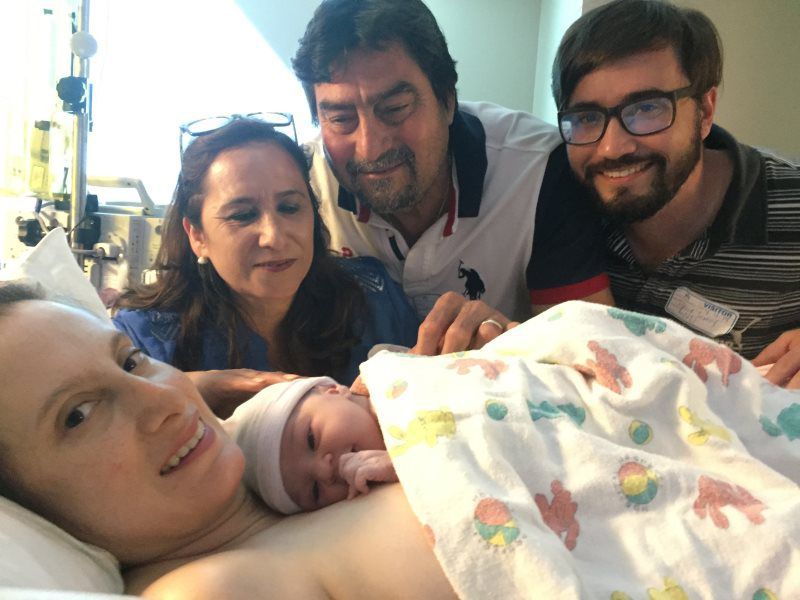 Newborn baby with mother and family in hospital room; all smiling.