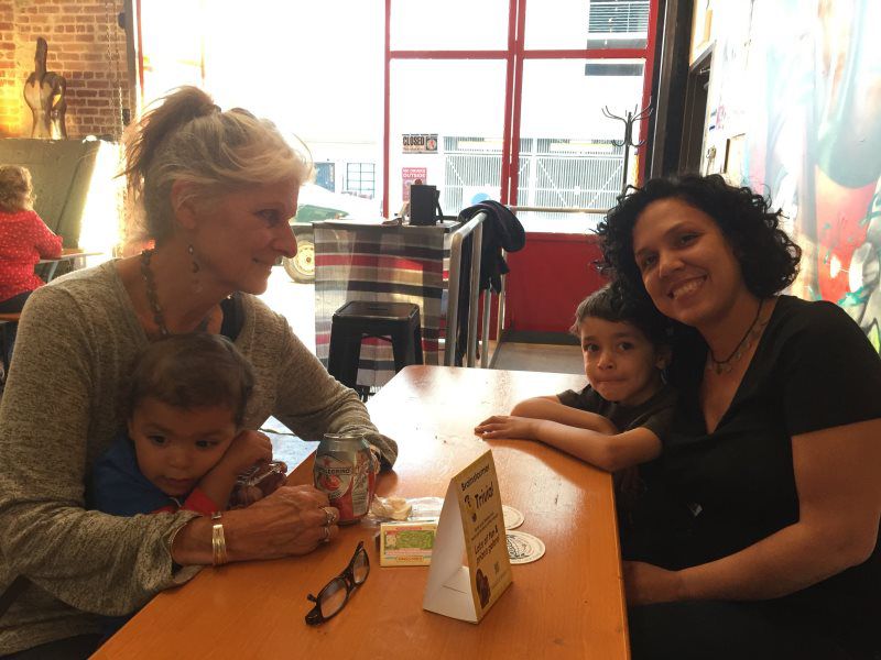 Two women and two children sit at a table in a cafe. The children rest on their arms.