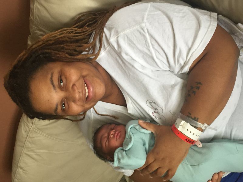 Woman smiling, holding newborn baby in hospital bed.