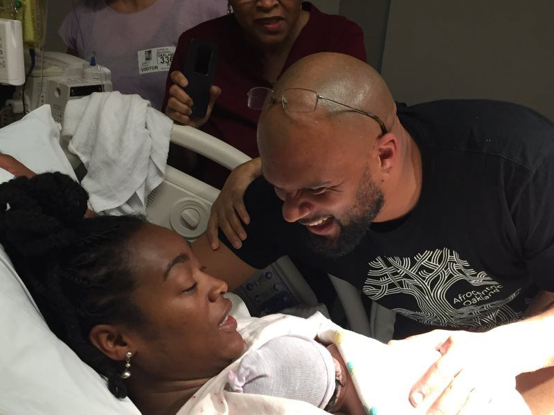 Woman giving birth in hospital, smiling man beside her. Nurse in background.