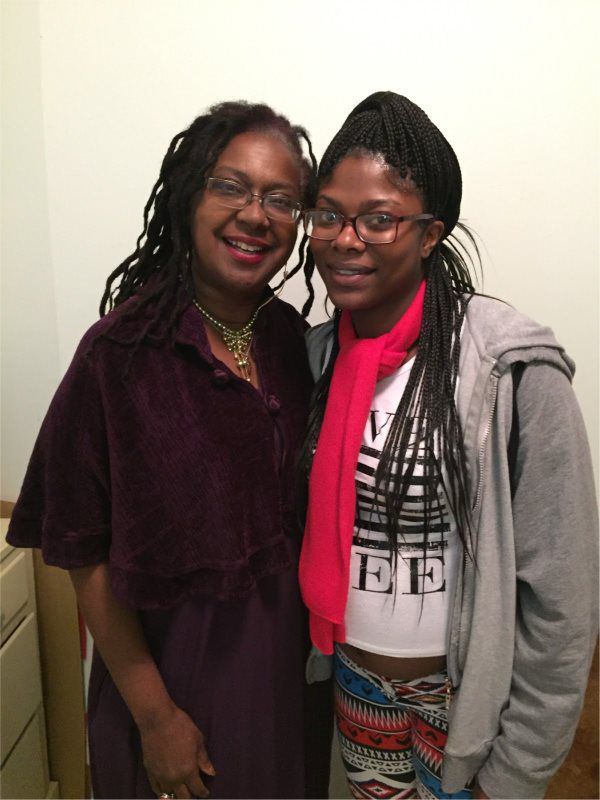 Woman in maroon and another in grey stand close, smiling.