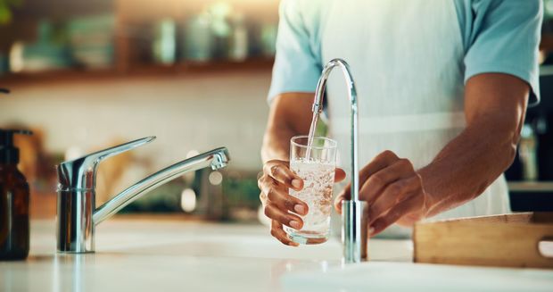 Person filling a glass with water at a kitchen sink from a running faucet Person filling a glass with water at a kitchen sink from a running faucet