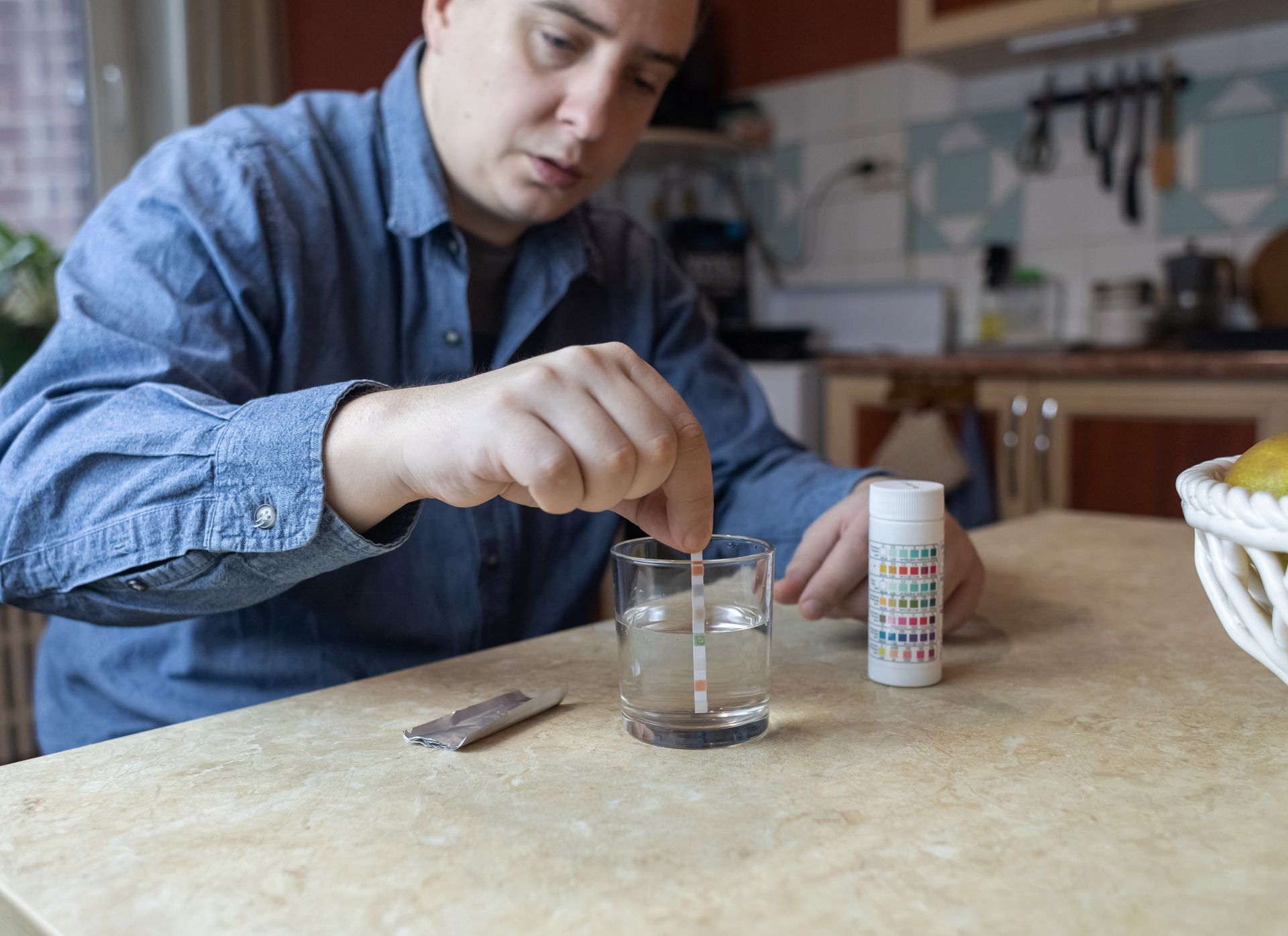 Person stirring a glass beaker on a kitchen counter beside a small labeled container and tools
