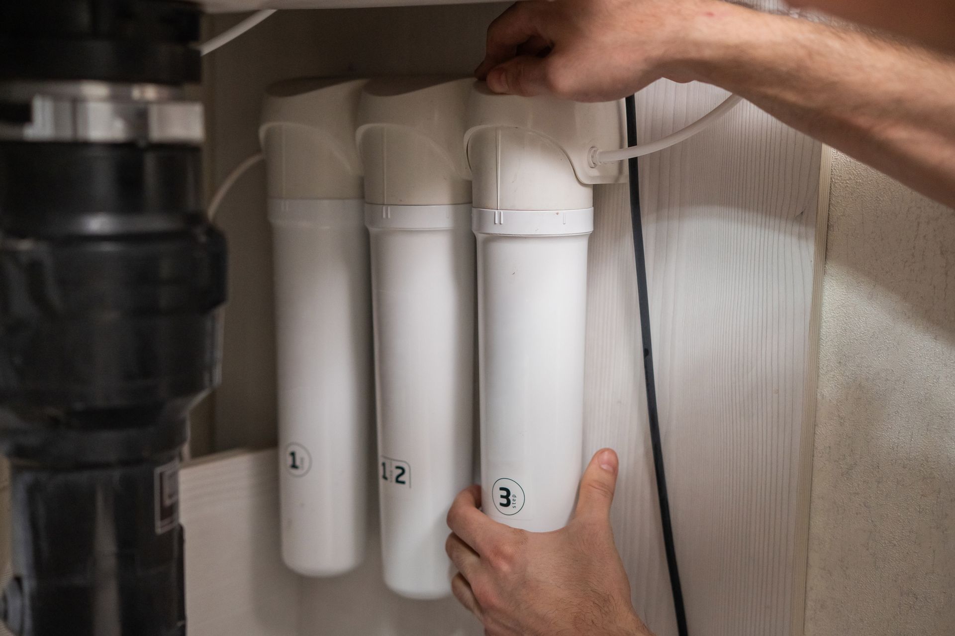 Hands installing white under-sink water filter cartridges labeled 1, 2, and 3. Hands installing white under-sink water filter cartridges labeled 1, 2, and 3.