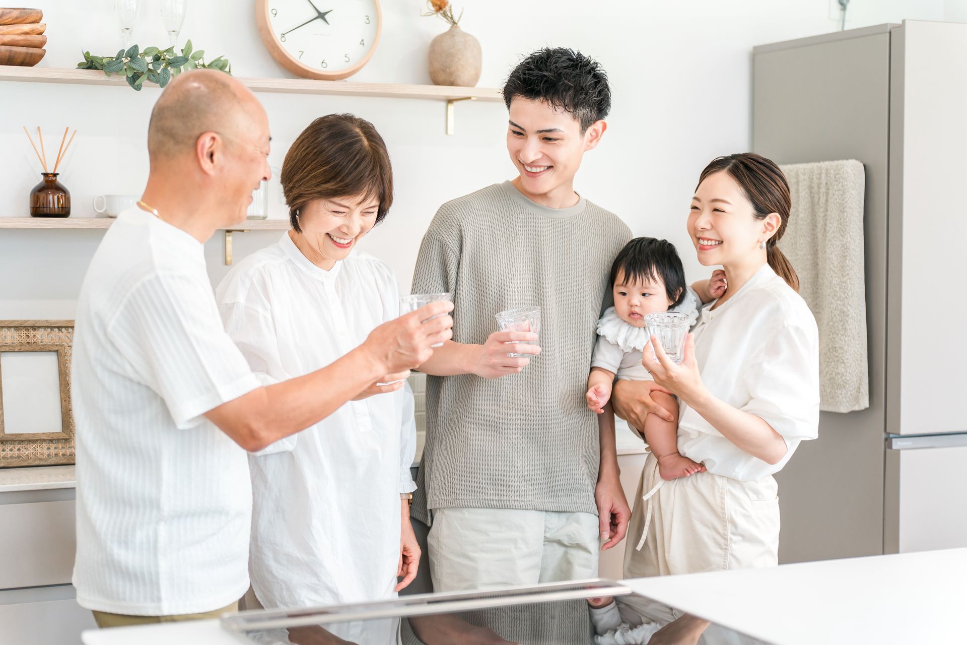 Family raising glasses together in a bright kitchen, smiling beside a baby. Family raising glasses together in a bright kitchen, smiling beside a baby.