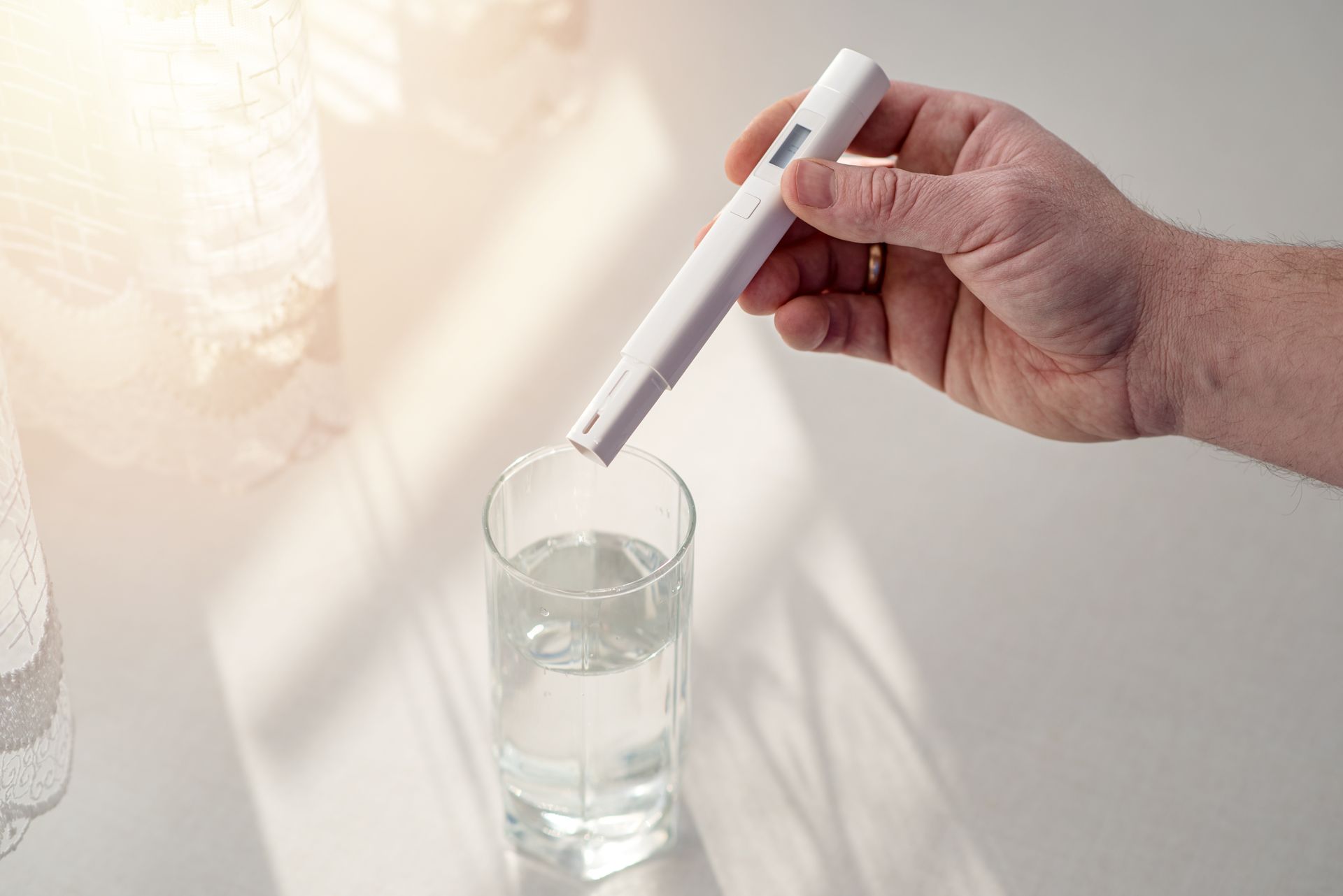 Hand holding a white thermometer over a glass of water on a bright table