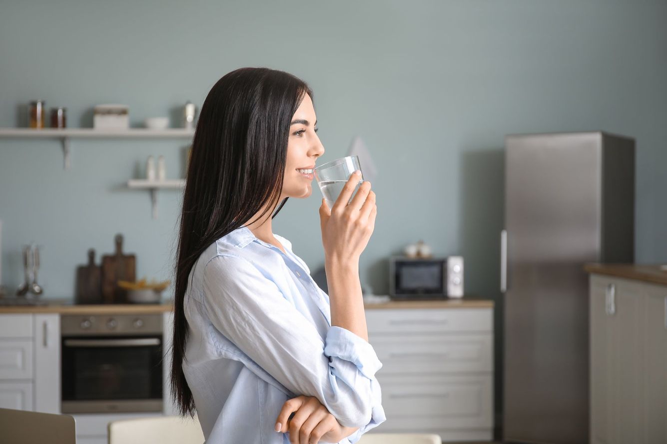 Woman in a kitchen holding a glass of water and looking out the window Woman in a kitchen holding a glass of water and looking out the window