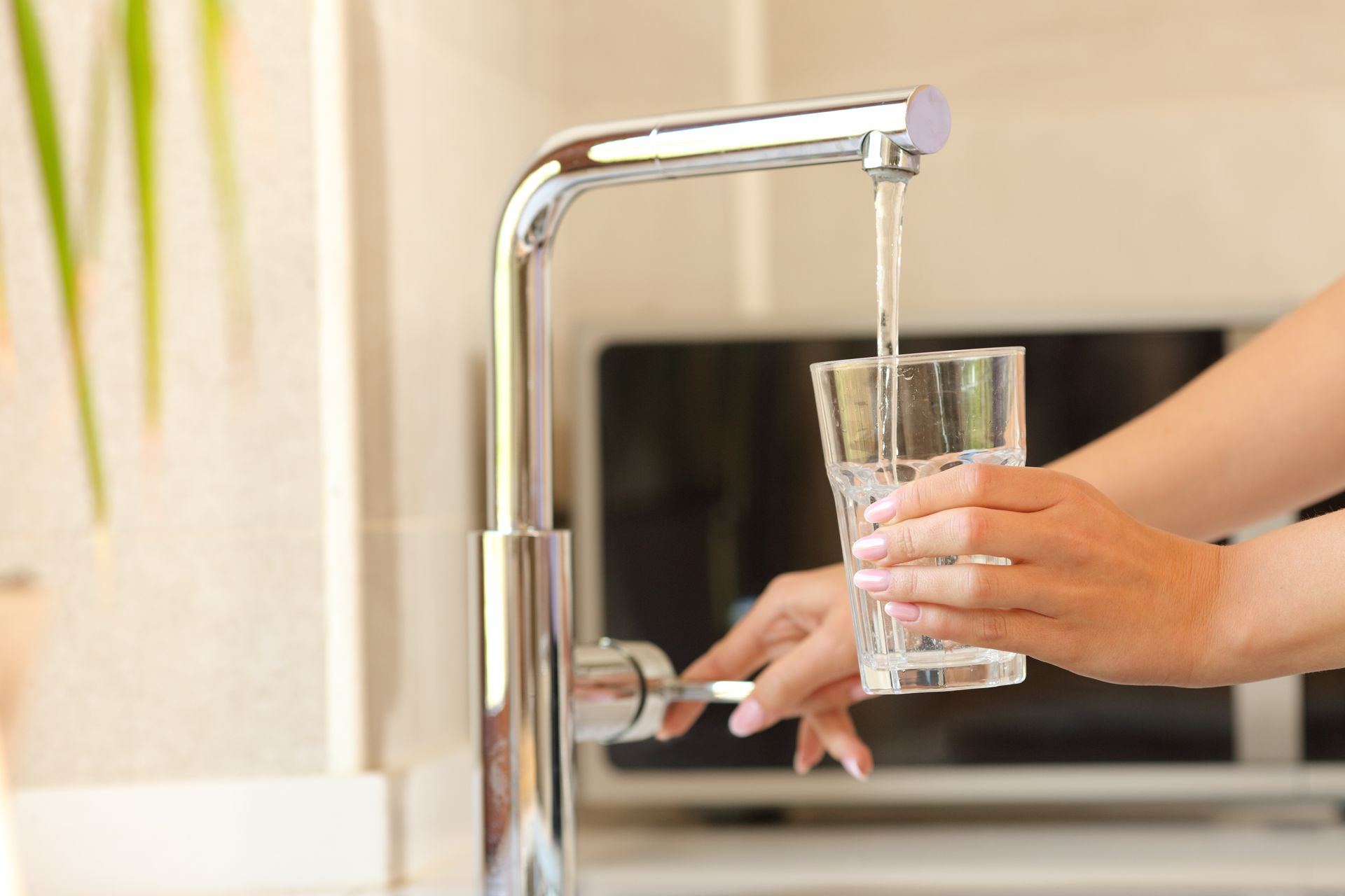 Hand filling a clear glass with water from a chrome kitchen faucet Hand filling a clear glass with water from a chrome kitchen faucet